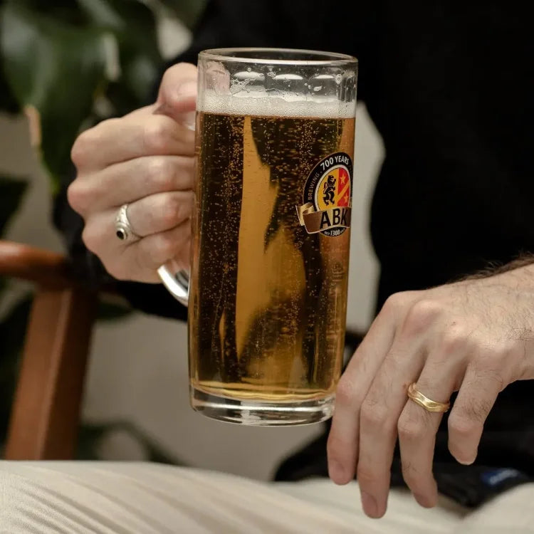 A man holds a pint glass filled with ABK hell beer