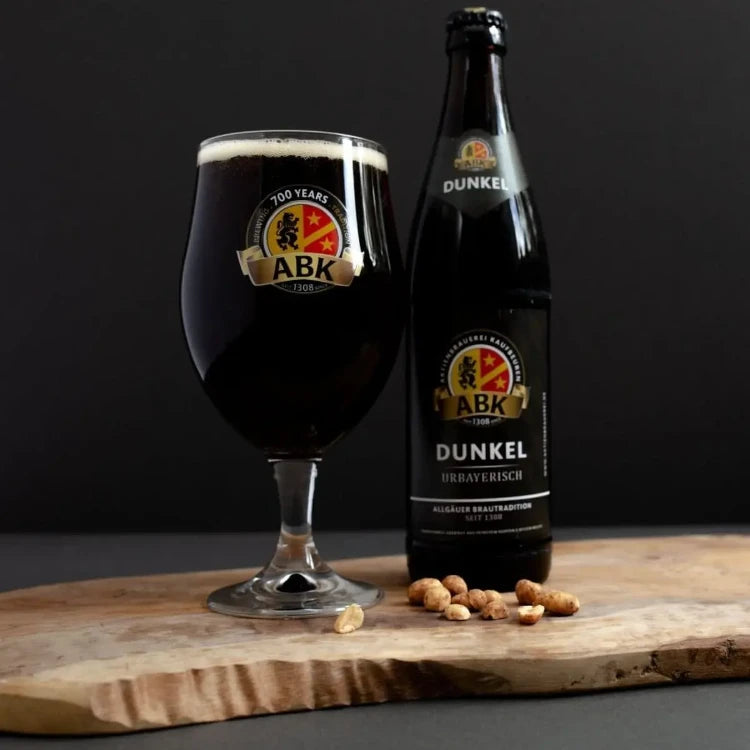 A bottle of ABK Dunkel and A munique glass with dunkel on a wooden board